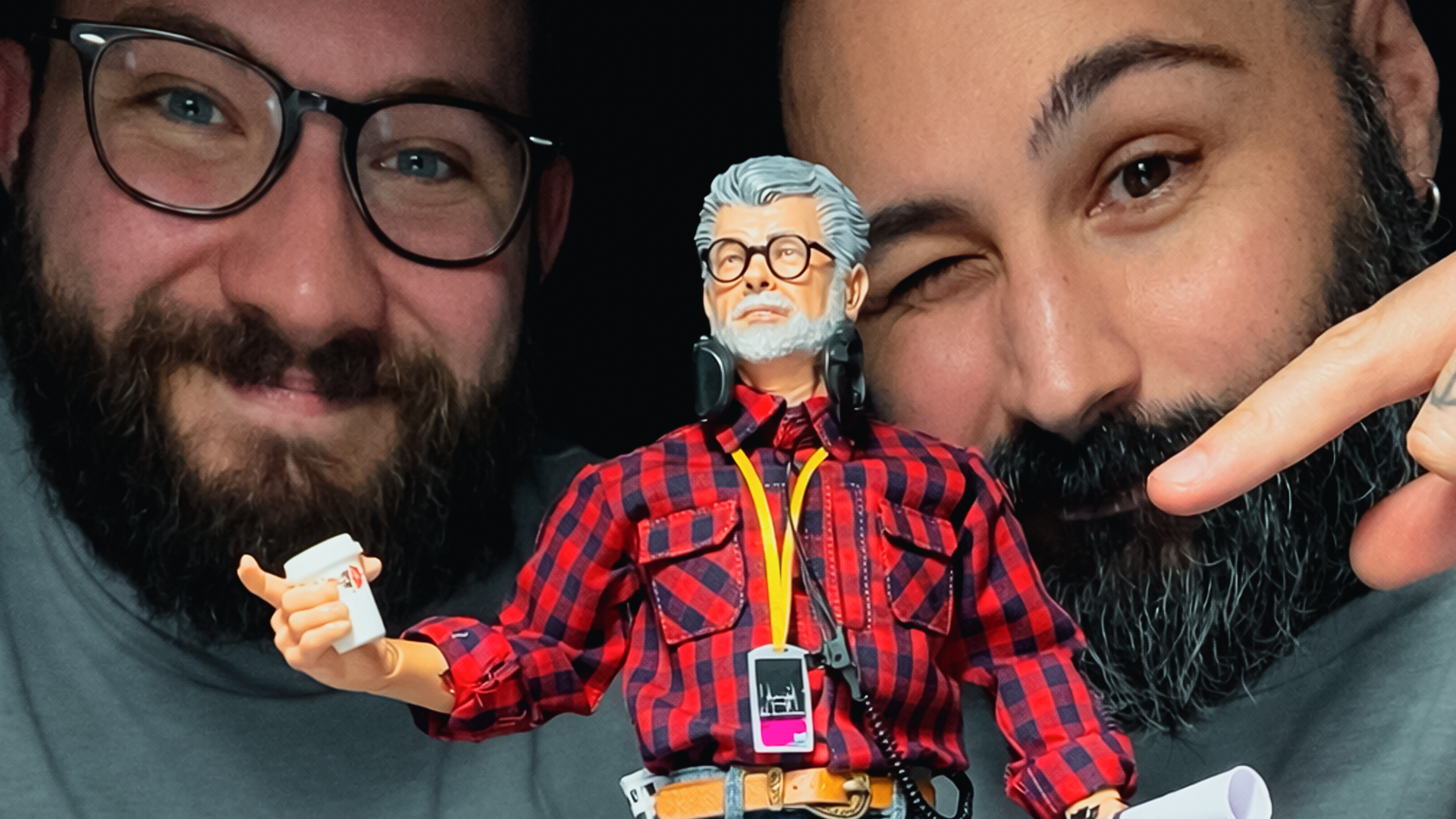 George Lucas 1:6 scale action figure fully dressed with plaid shirt, jacket, jeans, sneakers, and director accessories including coffee cup, headset, and production badge, displayed on custom stand.